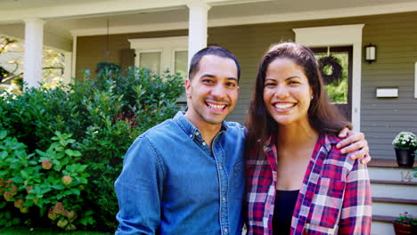 Portrait-Of-Smiling-Couple-Standing-In-Front-Of-Their-Home