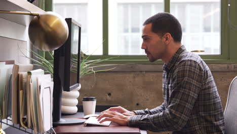 Young-Hispanic-man-using-computer-in-an-office,-side-view