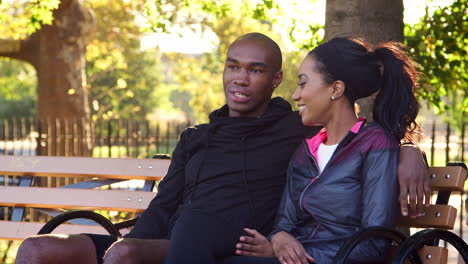 Young-black-couple-in-sports-clothes-talk-on-bench-in-a-park