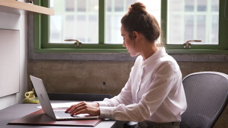 Young-woman-working-at-a-laptop-alone-in-an-office,-close-up