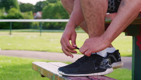 Male-runner-sitting-on-bench-tying-shoelaces,-low-section