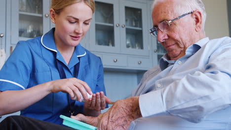 Nurse-Helping-Senior-Man-To-Organize-Medication-On-Home-Visit