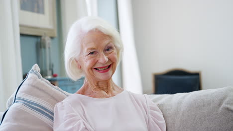 Portrait-Of-Smiling-Senior-Woman-Sitting-On-Sofa-At-Home