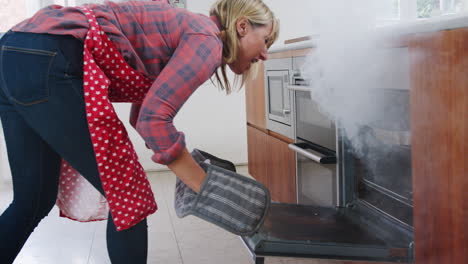 Mature-Woman-In-Kitchen-Takes-Burning-Meal-Out-Of-Oven
