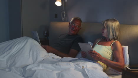 Senior-Couple-Wearing-Pajamas-Lying-In-Bed-Using-Digital-Devices