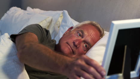 Sad-Senior-Man-Lying-In-Bed-Looking-At-Photo-Frame