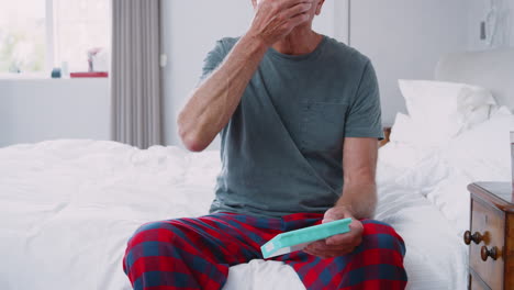 Senior-Man-Sitting-On-Bed-At-Home-Taking-Medication