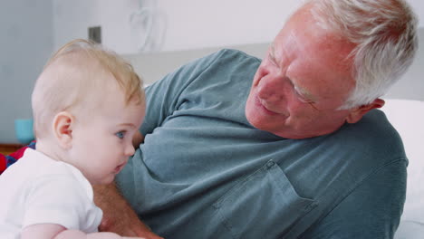 Grandfather-Lying-In-Bed-At-Home-Looking-After-Baby-Grandson