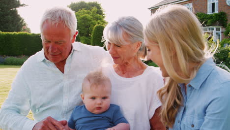 Grandparents-Sit-Outdoors-With-Baby-Grandson-And-Adult-Daughter