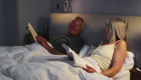 Senior-Couple-Wearing-Pajamas-Lying-In-Bed-Reading-And-Talking