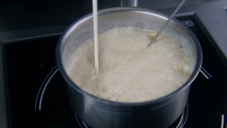 Cook-Mixes-Sauce-By-Whisk-and-Pours-Cream-in-Stewpan