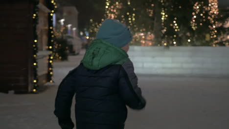 Child-running-in-snowy-street-with-Christmas-lights