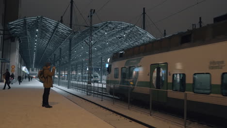 Mann-Macht-Mobiles-Video-Vom-Zug,-Der-Nachts-Am-Bahnhof-In-Helsinki-Ankommt