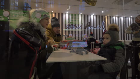 Familie-In-Winterkleidung-Sitzt-Im-Café-Und-Wartet-Auf-Die-Bestellung,-Finnland