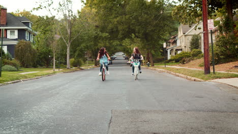 Two-teen-girls-riding-bikes-in-a-quiet-street,-front-view