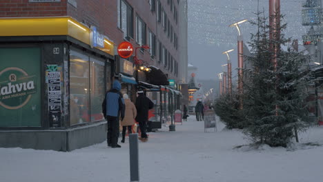 Snowy-street-with-stores-and-walking-people-in-Rovaniemi-Finland