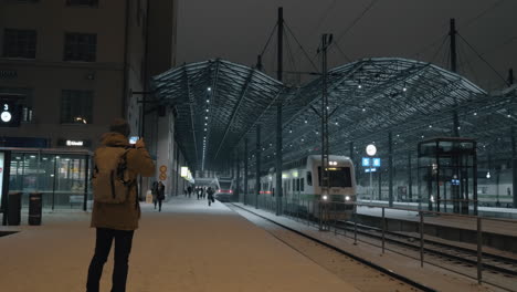 Mann,-Der-Ein-Mobiles-Video-Von-Einem-Zug-Aufnimmt,-Der-Nachts-Den-Bahnhof-In-Helsinki-Verlässt