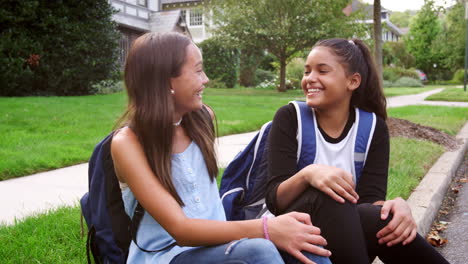 Two-teen-girlfriends-sit-at-the-roadside-smiling-to-camera
