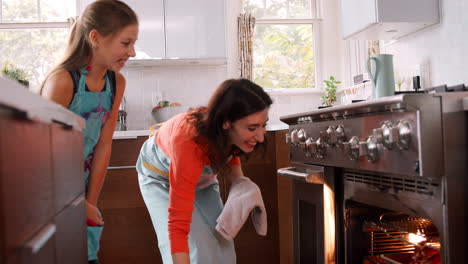 Mother-taking-bread-out-of-the-oven-while-daughter-watches