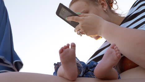 Mum-with-sleeping-baby-at-the-beach-Woman-using-cellphone