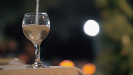 Pouring-white-wine-in-outdoor-restaurant-at-night