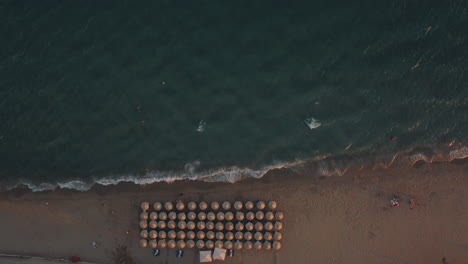 Aerial-shot-of-blue-sea-and-sunbeds-under-umbrellas-at-the-beach
