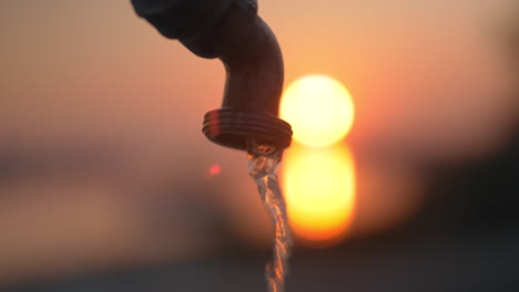 Water-running-from-the-tap-on-background-of-sunset
