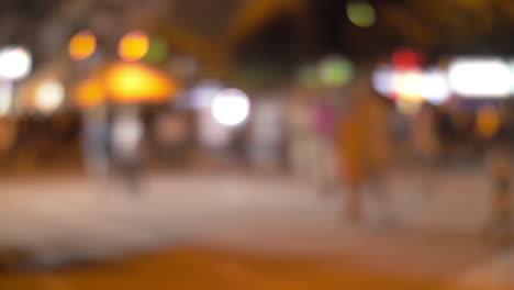 Calle-Nocturna-Iluminada-Con-Gente-Caminando-Desenfocada