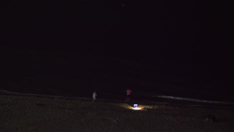 Nachtansicht-Von-Menschen,-Die-Sich-Am-Strand-Entspannen-Und-Auf-Das-Dunkle-Meer-Schauen