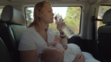 Mother-drinking-water-and-nursing-baby-in-the-car
