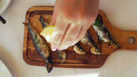 Pouring-lemon-juice-on-grilled-sardines
