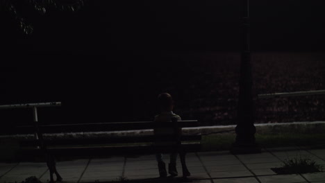 Lonely-kid-sitting-on-the-bench-outdoor-at-night