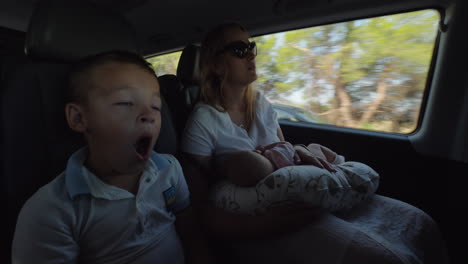 Mother-with-baby-and-elder-son-traveling-by-car-Boy-tired-and-yawning
