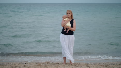 Mother-with-lost-look-holding-baby-being-alone-at-the-beach-near-sea
