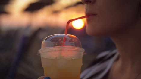 Frau-Trinkt-Bei-Sonnenuntergang-Am-Strand-Ein-Eisgetränk
