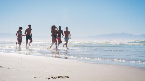Grupo-De-Amigos-Corriendo-Entre-Olas-En-Vacaciones-En-La-Playa