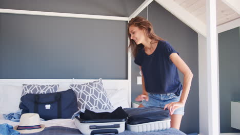 Woman-Trying-To-Close-Full-Holiday-Suitcase-In-Bedroom