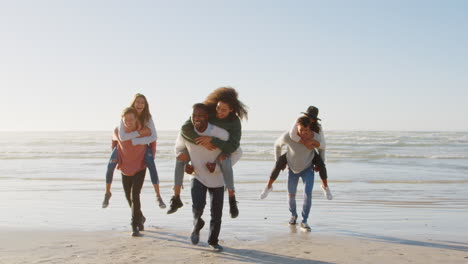 Group-Of-Friends-Having-Piggyback-Race-On-Winter-Beach-Together
