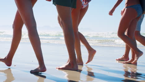 Close-Up-Of-Friends-Legs-Walking-Along-Shoreline-On-Beach-Vacation