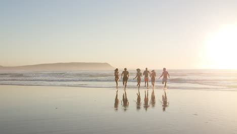 Friends-At-Sunset-Running-Along-Shore-On-Beach-Vacation