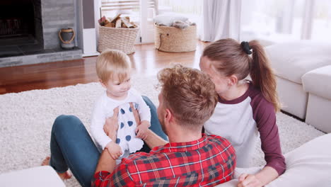 Young-couple-lifting-their-toddler-daughter-in-sitting-room
