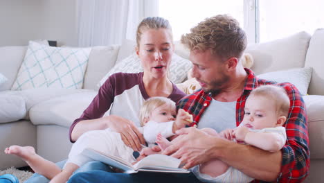 Young-white-couple-reading-book-with-two-toddlers,-side-view