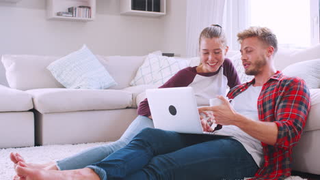 Young-white-couple-sitting-on-the-floor-at-home-using-laptop