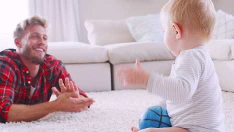 Young-father-lying-on-floor-clapping-with-toddler-son-at-home