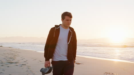 Young-Man-Walking-Along-Beach-As-Sun-Rises-Over-Ocean
