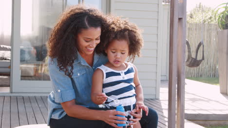 Mixed-race-mother-and-daughter-blowing-bubbles-in-garden