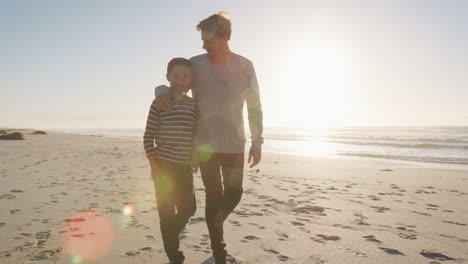 Father-With-Arm-Around-Son-Walking-Along-Winter-Beach