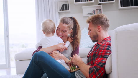 Young-couple-sitting-on-floor-and-embracing-daughter-at-home