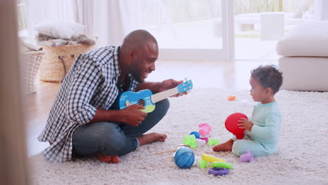 Young-black-father-palying-ukulele-with-son-in-sitting-room