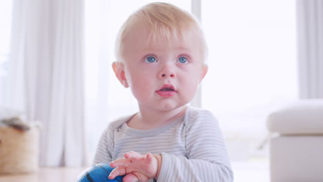 White-toddler-boy-sitting-on-floor-holding-ball,-close-up